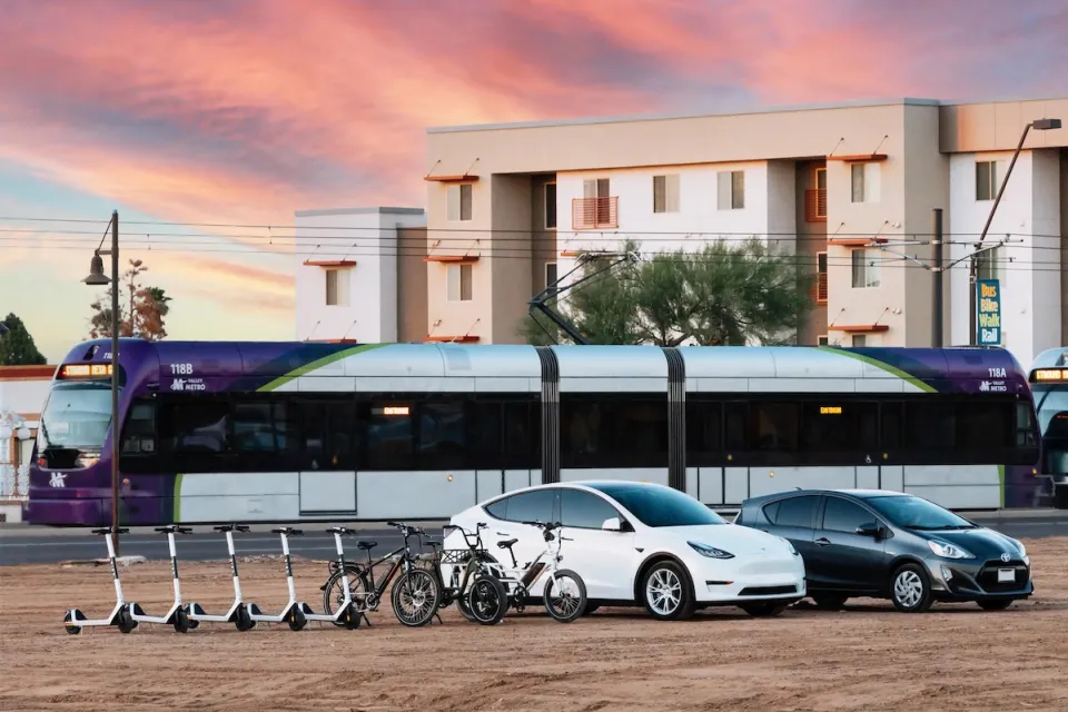Rendering of electric scooters, electric cars, light rail train, and apartments in background.